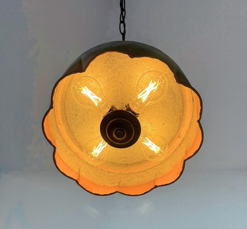 May include: A unique, hanging light fixture with a scalloped, flower-like shade. The shade is a warm, golden color with a dark, metallic rim. Four Edison-style light bulbs are visible inside the shade, creating a warm glow. The fixture hangs from a dark chain.