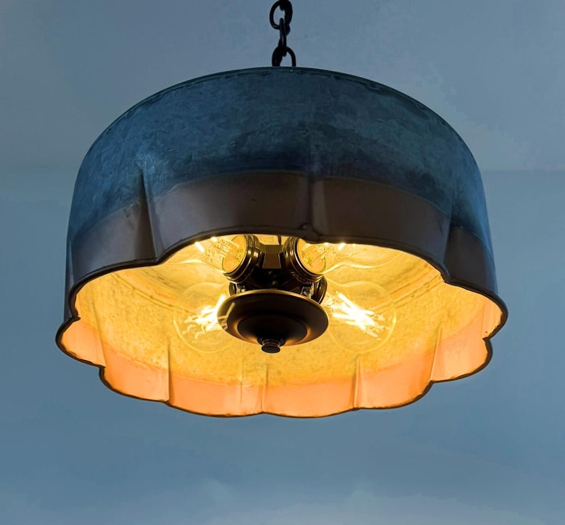 May include: A hanging pendant light with a galvanized metal shade and a copper-colored trim. The interior features exposed light bulbs, casting a warm glow. The fixture is suspended from a chain, offering a vintage or industrial aesthetic.