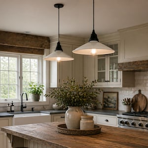 May include: Two pendant lights with white shades and black hardware hang above a wooden kitchen island. The kitchen features a farmhouse sink, white cabinets, and a window with natural light.