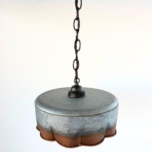 May include: A hanging pendant light with a galvanized metal shade and a copper-colored scalloped edge. The light fixture is suspended from a dark brown chain and has a simple, industrial design.