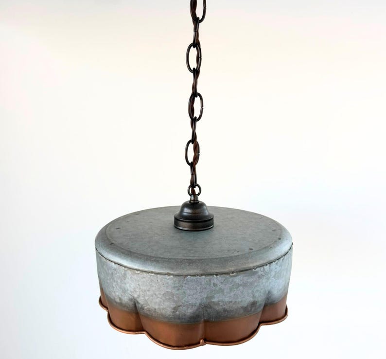 May include: A hanging pendant light with a galvanized metal shade and a copper-colored scalloped edge. The light fixture is suspended from a dark brown chain and has a simple, industrial design.