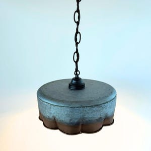 May include: A hanging pendant light with a galvanized metal shade and a dark chain. The shade has a scalloped edge with a two-tone finish, transitioning from a gray-blue to a brown color. The light fixture is suspended from the ceiling.