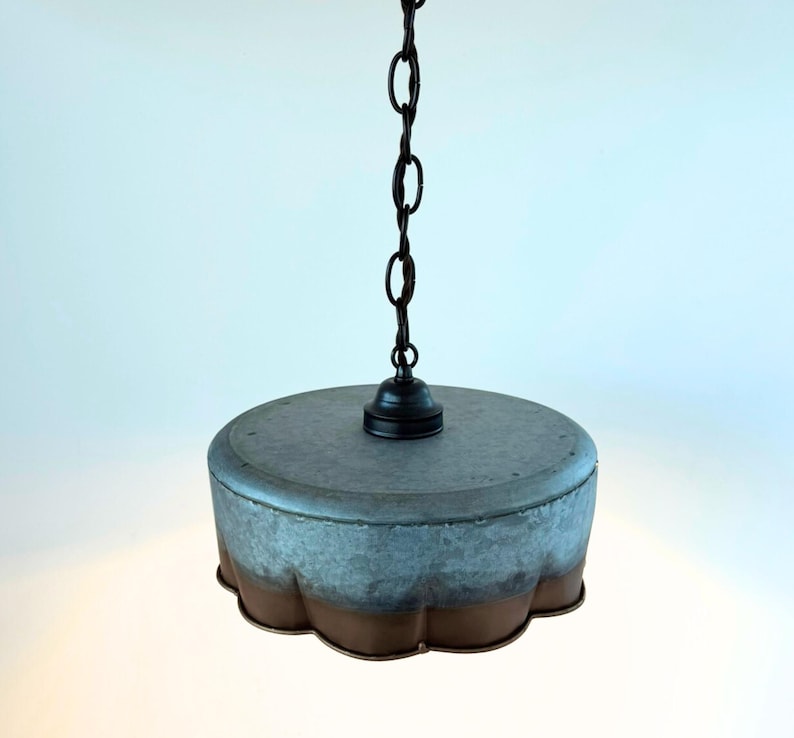 May include: A hanging pendant light with a galvanized metal shade and a dark chain. The shade has a scalloped edge with a two-tone finish, transitioning from a gray-blue to a brown color. The light fixture is suspended from the ceiling.