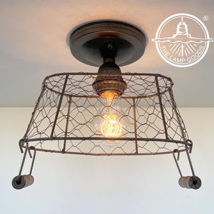 May include: A rustic ceiling light fixture made from a wire basket with a single light bulb. The fixture has a brown metal base and two wooden pulls.
