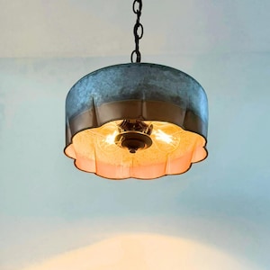 May include: A hanging light fixture with a galvanized metal shade and a scalloped, copper-colored trim. The fixture has two exposed light bulbs and a dark chain for hanging. The interior of the shade is a warm, off-white color.