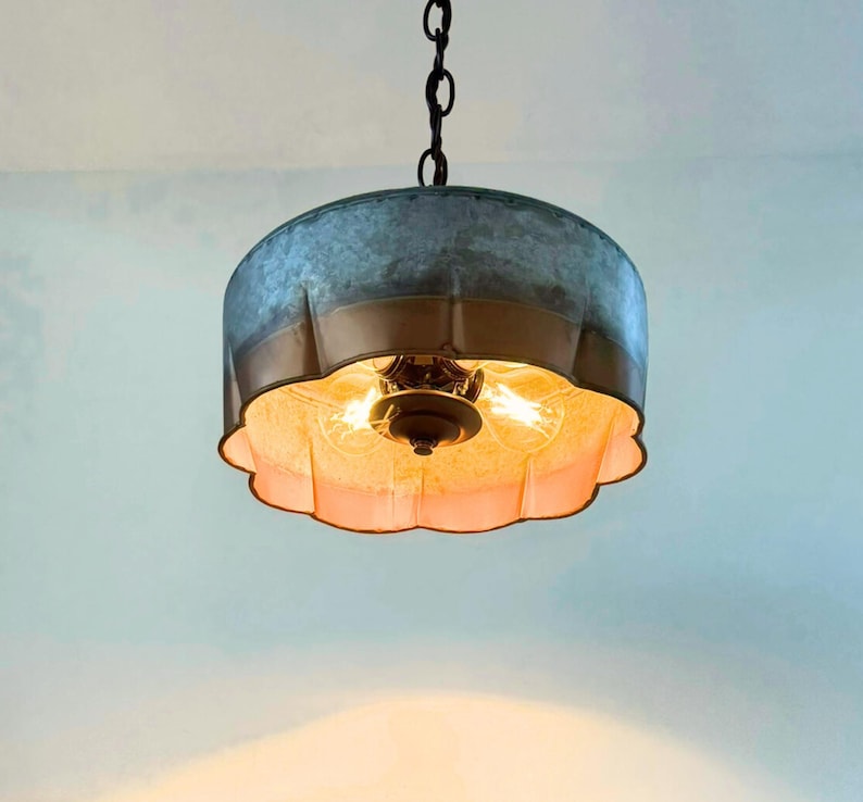May include: A hanging light fixture with a galvanized metal shade and a scalloped, copper-colored trim. The fixture has two exposed light bulbs and a dark chain for hanging. The interior of the shade is a warm, off-white color.