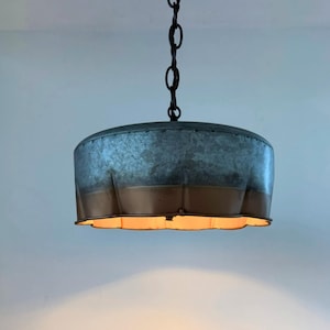 May include: A hanging pendant light with a galvanized metal shade and a bronze-colored lower band. The light fixture is suspended from a black chain. The shade has a scalloped edge, and the light is on.