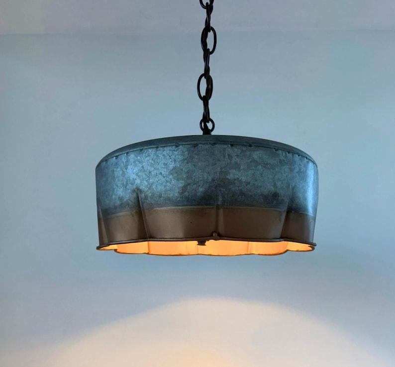 May include: A hanging pendant light with a galvanized metal shade and a bronze-colored lower band. The light fixture is suspended from a black chain. The shade has a scalloped edge, and the light is on.