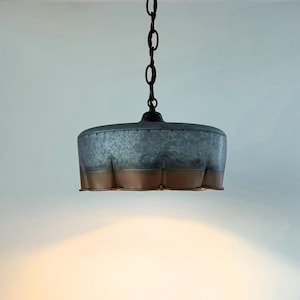 May include: A hanging pendant light with a galvanized metal shade and a copper-colored bottom edge. The light fixture is suspended from a black chain and is suitable for indoor lighting. The shade has a unique, textured appearance.