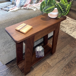May include: A dark brown wooden end table with a shelf. The table has a rounded edge and a simple design. A small wooden coaster and a crystal are on the shelf.