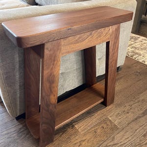 May include: A dark brown wooden end table with a single shelf. The table has a curved top and a simple, modern design.