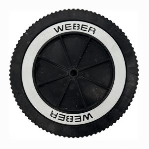 May include: A black wheel featuring a white circular band with the word "WEBER" in white. The wheel has a ridged outer edge and a central hub. It's likely a replacement part for a barbecue or outdoor cooking equipment.