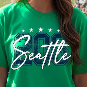 May include: Irish green t-shirt with the word "Seattle" in a white script font. Above the word "Seattle" are the numbers "206" in a dark blue block font, with five white stars above the numbers. The shirt is short-sleeved.
