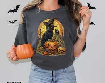 May include: Dark gray t-shirt featuring a Halloween design. The graphic includes a black cat wearing a witch hat, pumpkins, and a spooky castle. The word "PEPPER" is printed at the bottom.