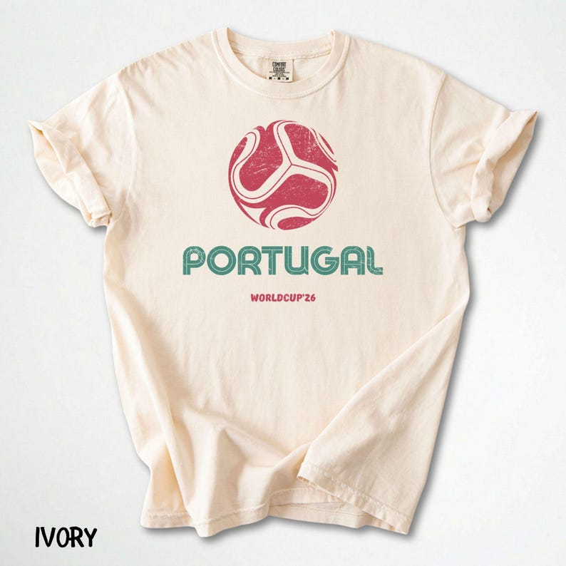 May include: Cream-coloured t-shirt with a distressed red and white football graphic. Below the graphic, the word "PORTUGAL" is printed in teal, with "WORLDCUP'26" underneath. The word "IVORY" is printed at the bottom.