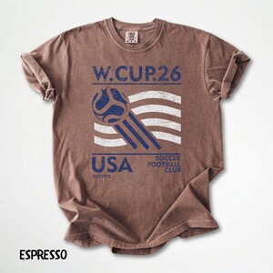 Close up of an espresso brown t-shirt with a white and blue vintage style USA Soccer Football Club print and soccer ball illustration.