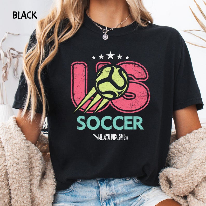 Model wearing a black Comfort Colors 1717 t-shirt with a distressed US Soccer W.CUP.26 graphic print on the front.