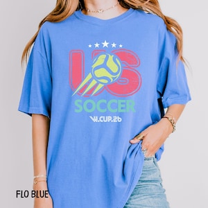 A model in a flo blue oversized t-shirt featuring the US Soccer graphic, paired with denim jeans for a casual look.
