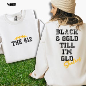 May include: White sweatshirt with the text "THE 412" in black and yellow. The back of the sweatshirt features the text "BLACK & GOLD TILL I'M OLD Steelers" in black and yellow. The sweatshirt is displayed on a green grassy surface.