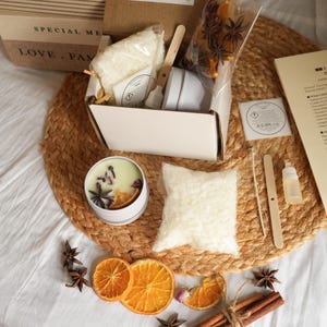 May include: Candle making kit with a white tin candle, dried orange slices, star anise, and cinnamon sticks. The kit includes wax, a small spatula, and a label that reads "Candle Making Kit".