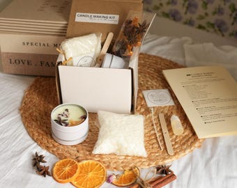 May include: A candle-making kit with a cardboard box, a white tin candle, and various ingredients. The kit includes wax, dried orange slices, star anise, cinnamon sticks, and instructions. The box is labeled "Candle Making Kit."