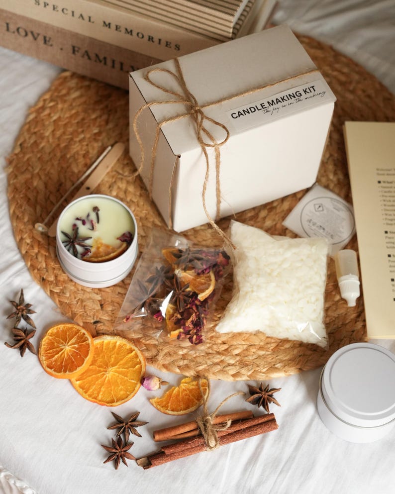 May include: A candle-making kit with a white box tied with twine, a candle tin, and ingredients like dried orange slices, star anise, and wax. The kit includes the text "Candle Making Kit" and "the joy is in the making."