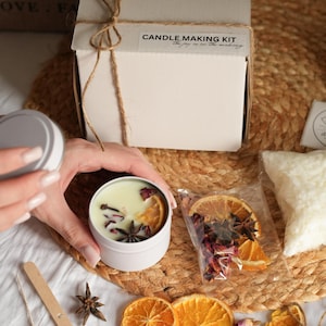 May include: A candle making kit with a white box tied with twine. The kit includes a white candle tin with dried orange slices, star anise, and rose petals. The text on the box reads "Candle Making Kit".