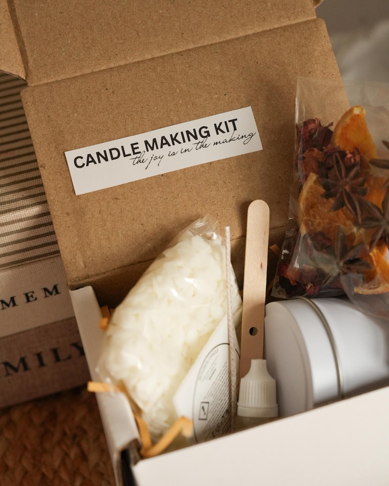 May include: A candle making kit in a brown cardboard box. The kit includes a bag of wax, a wooden stirring stick, a bottle, and a white container. A label on the box reads "CANDLE MAKING KIT the joy is in the making".