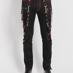Può includere: Pantaloni neri con cuciture e dettagli rossi, con più tasche e catene decorative. I pantaloni hanno un classico design a cinque tasche con cinghie e hardware in metallo. I pantaloni sono abbinati a scarpe in pelle nera.