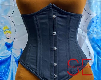 Puede incluir: Un corsé gris oscuro con cierres plateados. El corsé se exhibe en un maniquí con un torso bronceado. El corsé tiene costuras verticales y un borde inferior puntiagudo. El fondo presenta un patrón azul y blanco.