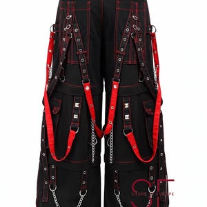 Puede incluir: Pantalones negros de pierna ancha con costuras rojas en contraste, m&uacute;ltiples bolsillos cargo, anillas en D de metal plateado, tachuelas piramidales y correas de tela roja extra&iacute;bles. La prenda incluye cadenas plateadas y el logo STORE OF EUROPE.