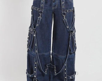 May include: Dark wash denim cargo pants with multiple pockets, silver grommets, and adjustable straps. The wide-leg pants feature a drawstring waist and decorative metal hardware. The pants have a unique, edgy style.