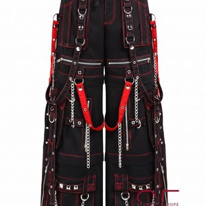 Op de afbeelding: Zwarte cargobroek met rode contraststiksels, meerdere utility-zakken, zilverkleurige metalen kettingen, D-ringen en verstelbare banden. De broek heeft een taille met trekkoord, vakken met ritssluiting en zilveren studs op de onderste zakken.