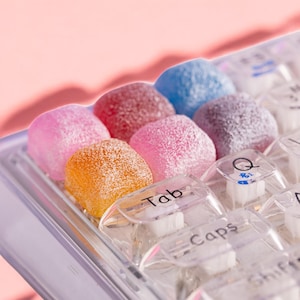 May include: A close-up of a clear keyboard with colourful candy-like keycaps. The keycaps are pink, blue, orange, and red. The keys are labelled "Tab", "Caps", "Q", and "Shift".