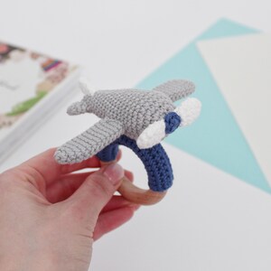 May include: A gray and blue crocheted airplane rattle with a wooden ring. The airplane has white propeller blades.