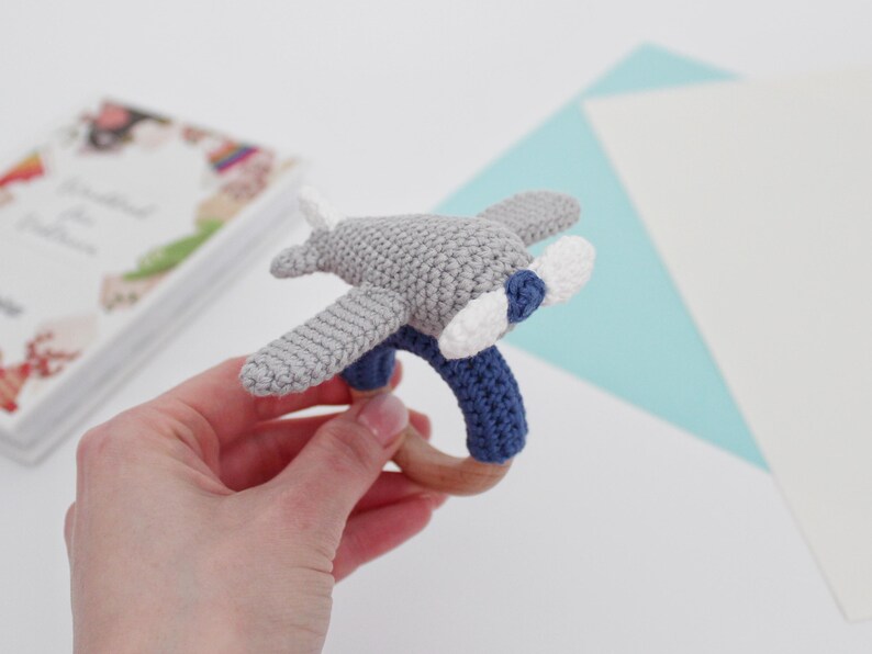 May include: A gray and blue crocheted airplane rattle with a wooden ring. The airplane has white propeller blades.