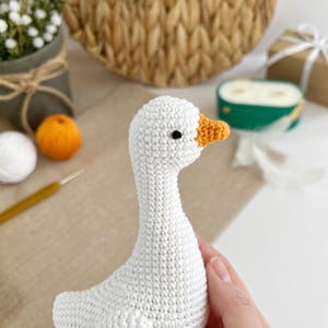 May include: A handmade white crochet goose with an orange beak and black eyes. The goose is a soft, plush toy, perfect for nursery decor or as a unique gift. The crochet stitches are visible, adding to the handcrafted charm.