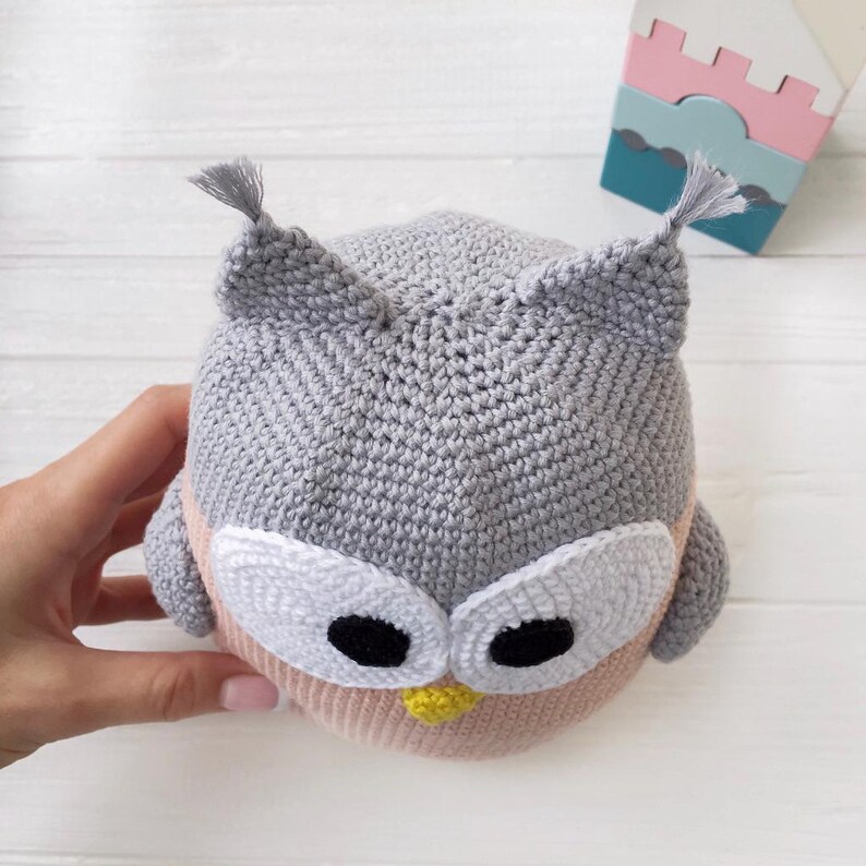 May include: A gray and pink crocheted owl plush toy with white eyes and a yellow beak.