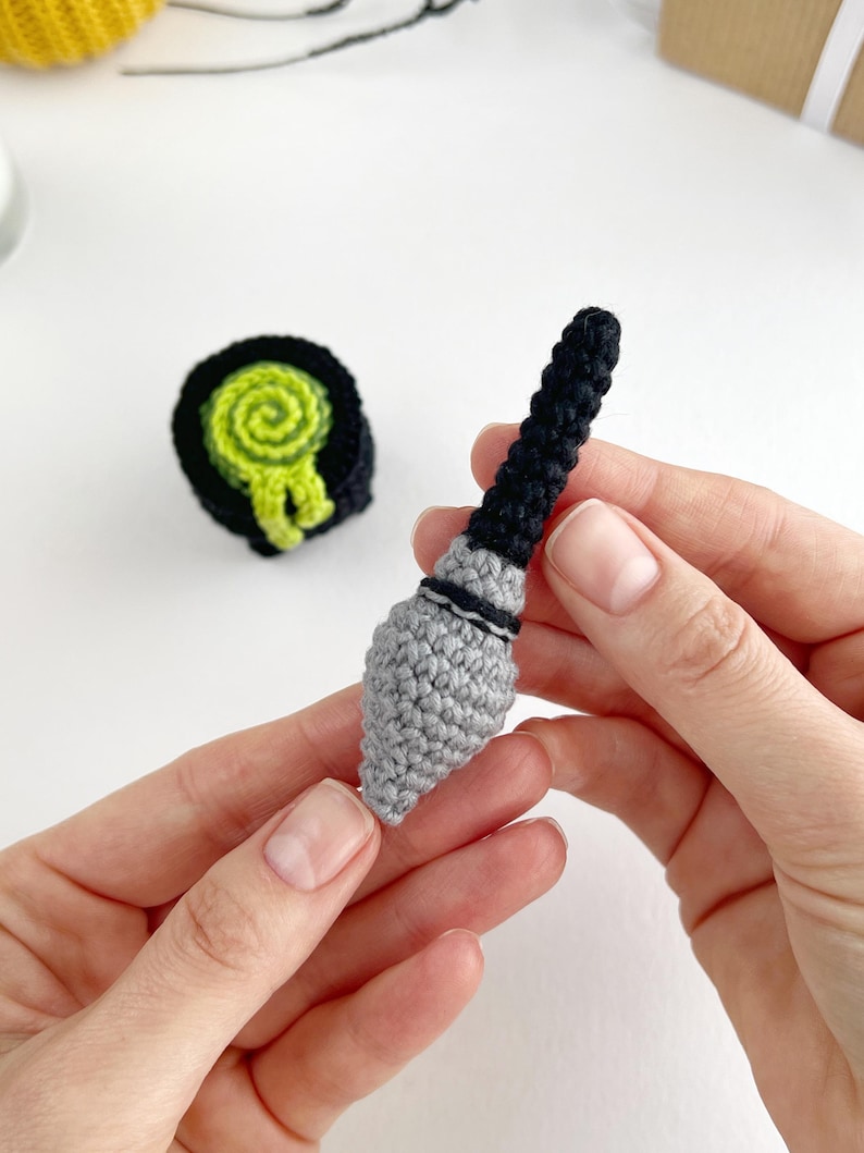May include: A small, handcrafted crochet kunai weapon featuring a grey pointed blade and a black handle, accompanied by a separate circular black and lime green crochet scroll or target object with a spiral pattern on its top surface.