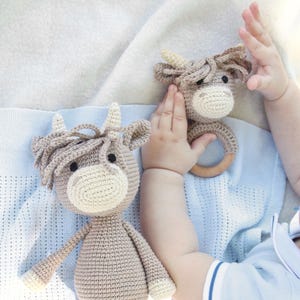 Puede incluir: Dos peluches de vaca de crochet marr&oacute;n y blanco. Uno es un peluche m&aacute;s grande con una postura de pie. El otro es un peluche m&aacute;s peque&ntilde;o con un anillo de madera unido a su cabeza.