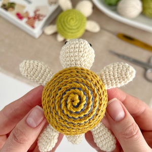 Puede incluir: Tortuga de ganchillo hecha a mano con cabeza y extremidades de color crema, y caparaz&oacute;n amarillo con dise&ntilde;o de espiral azul. La tortuga es un art&iacute;culo encantador y hecho a mano. Otras tortugas y materiales de artesan&iacute;a est&aacute;n en el fondo.