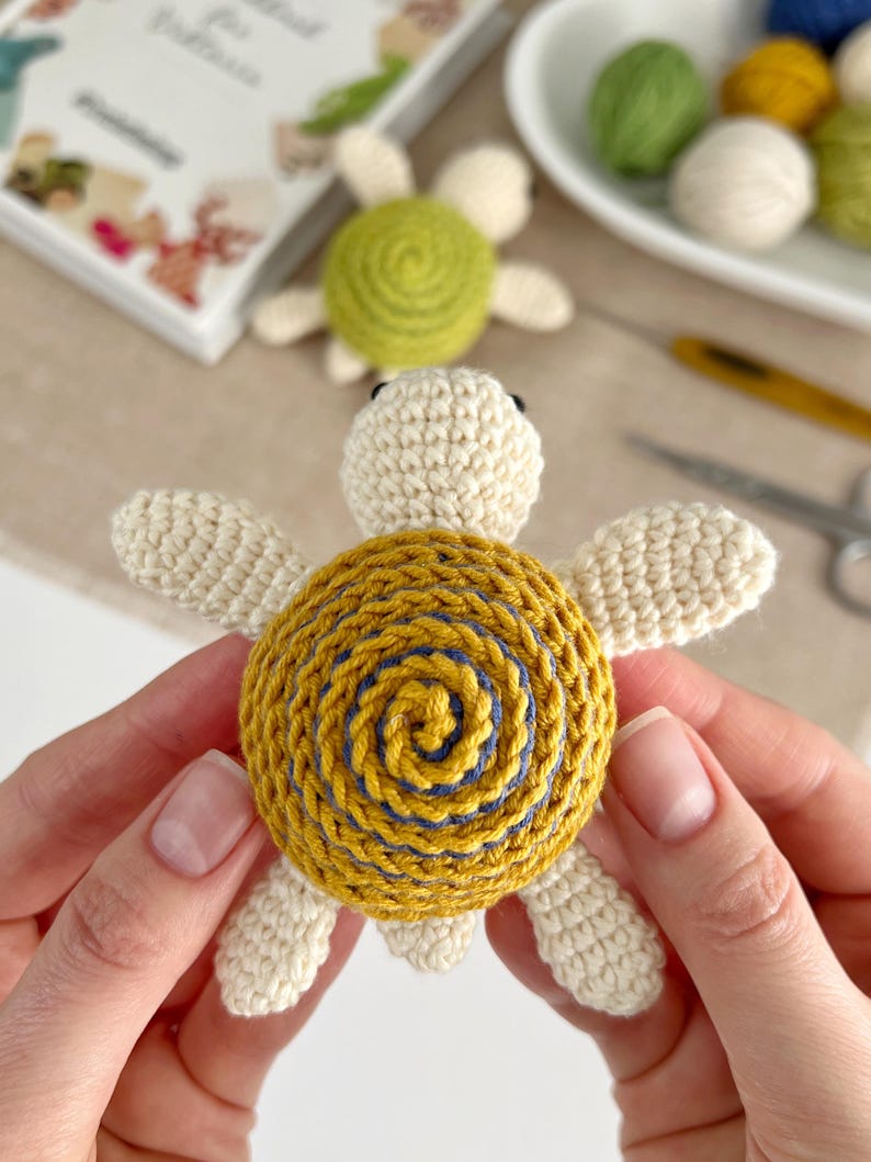 Puede incluir: Tortuga de ganchillo hecha a mano con cabeza y extremidades de color crema, y caparaz&oacute;n amarillo con dise&ntilde;o de espiral azul. La tortuga es un art&iacute;culo encantador y hecho a mano. Otras tortugas y materiales de artesan&iacute;a est&aacute;n en el fondo.