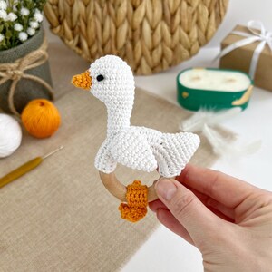 May include: White crocheted goose rattle with orange feet attached to a wooden ring.