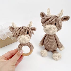 Puede incluir: Dos peluches de vaca Highland de crochet marr&oacute;n y blanco. Uno es un peluche m&aacute;s grande y el otro es un peluche m&aacute;s peque&ntilde;o unido a un anillo de madera.