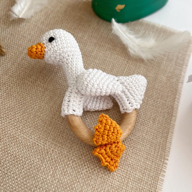 May include: A white crocheted goose with orange crocheted feet attached to a wooden teething ring.