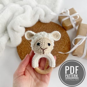 May include: Crochet amigurumi lamb rattle toy with a wooden ring. The lamb is white with black eyes and a brown nose. The toy is perfect for babies and toddlers.