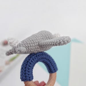 May include: A gray crocheted airplane toy attached to a blue crocheted ring with a wooden teething ring.
