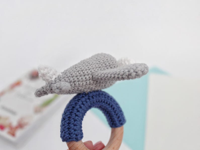 May include: A gray crocheted airplane toy attached to a blue crocheted ring with a wooden teething ring.