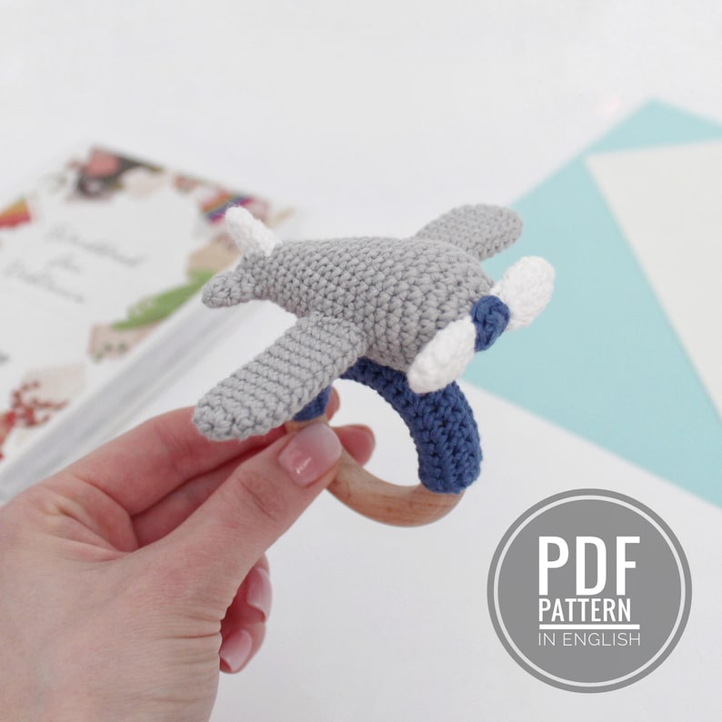 May include: A crochet airplane rattle with a wooden ring. The airplane is gray with blue and white details. The rattle is a great toy for babies.
