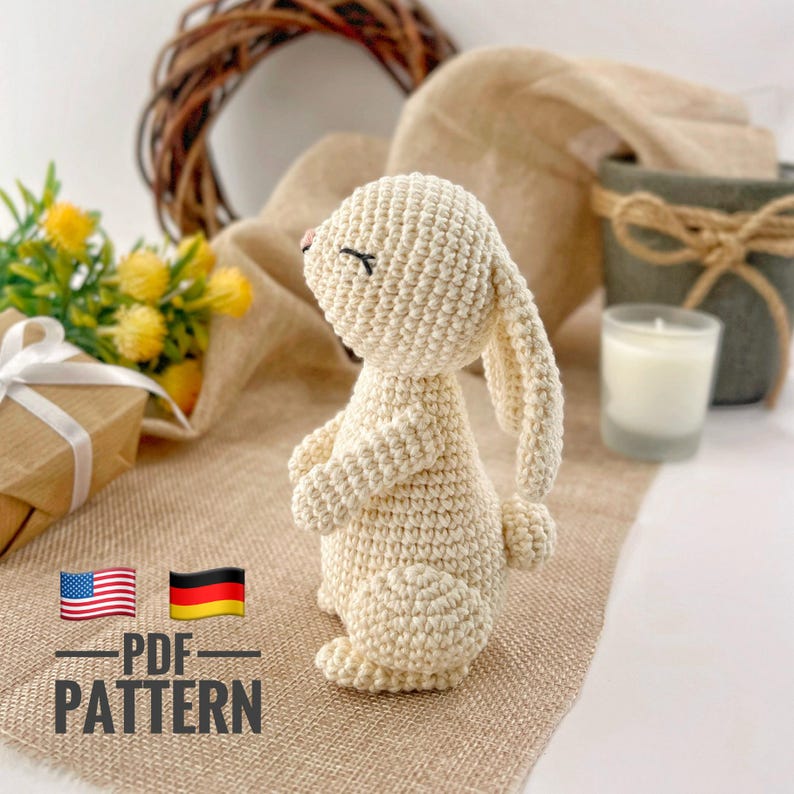 May include: A crocheted white bunny rabbit amigurumi toy with closed eyes. The bunny is sitting on a brown burlap surface. The image includes the text "PDF PATTERN" in black and white.